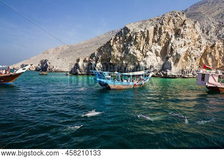 Khasab, Oman - Feb 9, 2022: Dolphins And Tourist Boats Near Fjords, Musandam Peninsula.