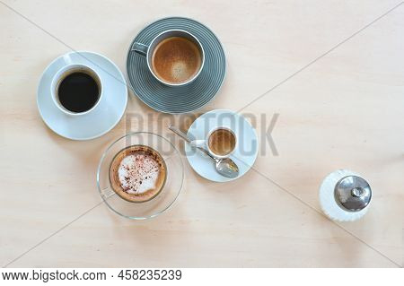 Various Coffee Drinks Like Espresso, Cappuccino, Lungo Black And With Crema And A Sugar Dispenser On