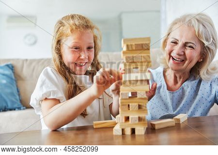 Grandmother And Granddaughter Aplaying With Wooden Brick Toy At Home