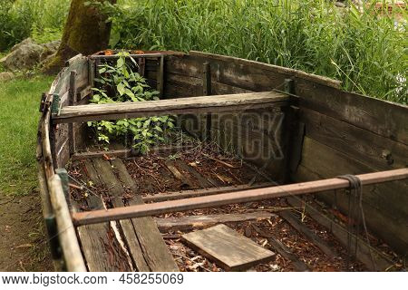 An Old Broken Wooden Ship On The Shore Overgrown With Grass