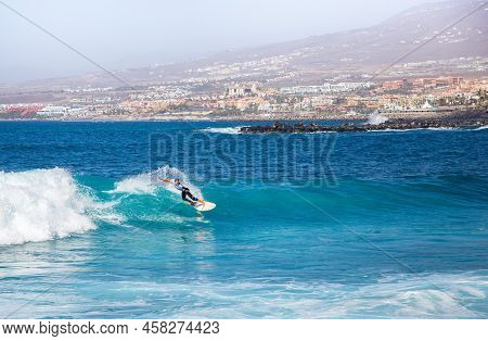 Costa Adeje, Spain - February 8, 2019: Surfer Girl On A Ocean Wave Against The Background Of A Popul