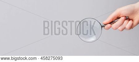Magnifying Lens In Hand On Gray Banner With Copy Space For Text.