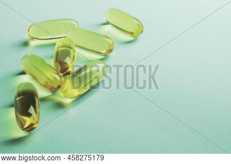 Yellow Softgels Lie On A Green Surface. Fish Oil. Vitamins And A Healthy Lifestyle. Background Or Ba