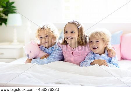 Kids Play In Bed. Children At Home In White Sunny Bedroom. Brother And Sister In Matching Pajamas Pl