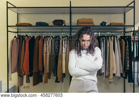 Upset And Sad Young Woman Standing In A Clothing Store In A Shopping Center, Hands Folded, Dissatisf