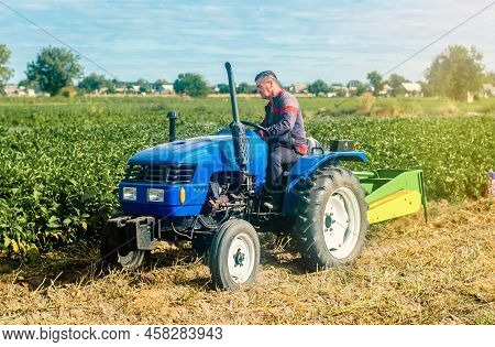 Middle-aged Farmer On A Tractor. Work On Agricultural Machinery On The Field. Harvest Potatoes. Farm