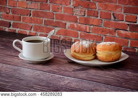 A Cup Of Hot Coffee On A Saucer With A Spoon And A Plate With Two Donuts Covered In Powdered Sugar O