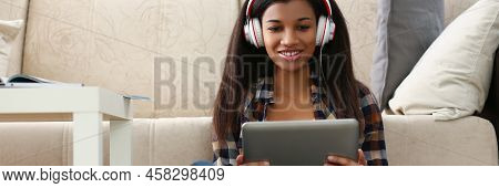 Low Angle Of Latin Young Woman Sit On Carpet With Tablet And Watch Show, Lady In Headset. Spend Time
