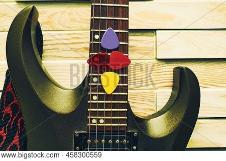 Black Electric Guitar With Plectrums In Strings On A Wooden Block Background