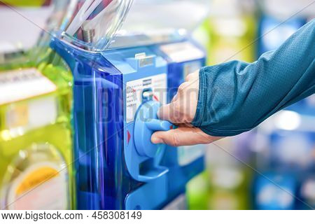 A Human Hand In A Turquoise Sweater Is Twisting A Blue Gashapon Machine To Release A Figure. In Japa