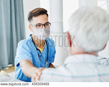 Doctor Or Male Caregiver With Senior Man Wearing Protective Mask At Home Or Nursing Home