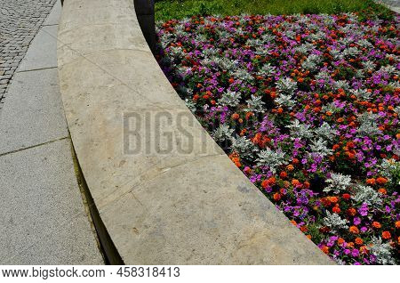 Crazy Annual Bed With A Pink-orange Combination Of Flowers. Large Retaining Walls Of Rounded Sandsto