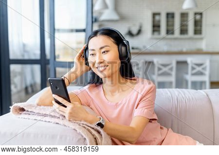 Attractive Asiatic Woman With Dark Hair And Snow-white Smile, Listening Her Favorite Song With Headp