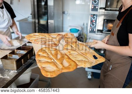 A Woman In A Bakery Takes Traditional French Fougasse Bread Out Of The Oven. Front View.