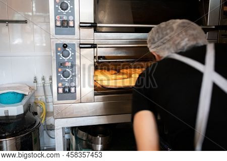 A Woman In A Bakery Takes Traditional French Fougasse Bread Out Of The Oven. Front View.
