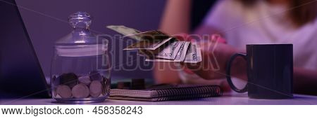 Close-up Of Broken Young Woman Counting Cash Money, Glass Container With Coins On Desk . Saving Up F