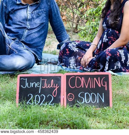 Indian Couple Posing For Maternity Baby Shoot. The Couple Is Posing In A Lawn With Green Grass And T