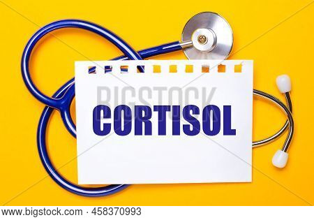 On A Bright Yellow Background, A Blue Stethoscope And A Sheet Of Paper With The Text Cortisol. Medic