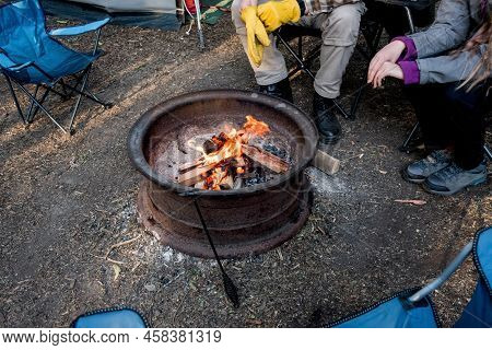 Campfire Burning In A Firepit . People Sitting Around The Campfire. Camping Life. Outdoor Family Rec
