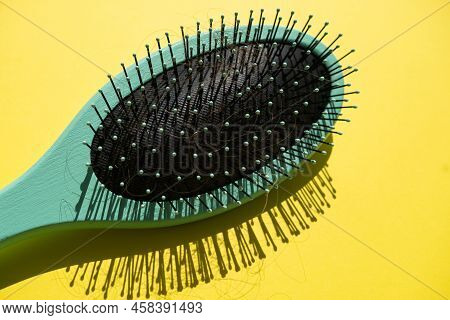 Green Comb And Fallen Hair On The Yellow Background. Baldness And Hair Loss Problem