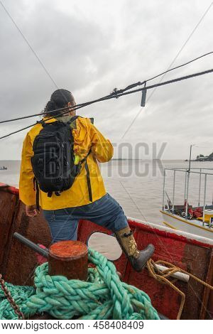 Vertical Photo Of A Latin Fisherman With Raincoat Checking The Weather Forecast On His Cell Phone On