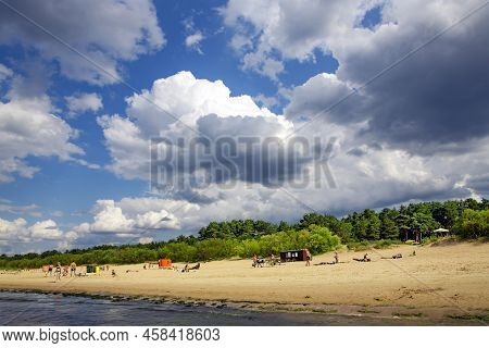 Latvia, Vecaki, July, 2022: Cumulus Clouds Over Wild Sandy Coast Where Vacationers Sunbathe On The S