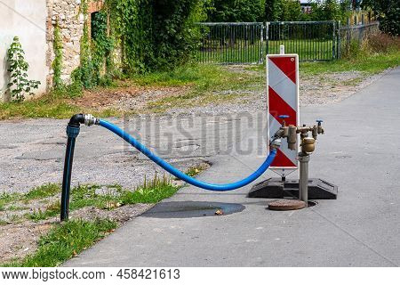 Standpipe With Connected Blue Hose On A Pedestrian Sidewalk. Red And White Plastic Barrier.