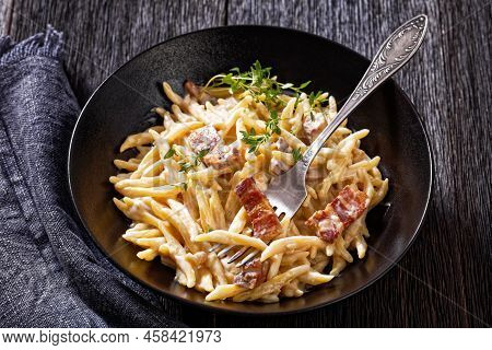 Capunti Pasta In Cream Pecorino Cheese And Pancetta Sauce In Black Bowl On Dark Wooden Table, Close-