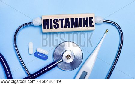 On A Light Gray Background, A Stethoscope, An Electronic Thermometer, Pills, A Wooden Block With The