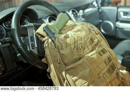 A Handgun Half Zipped In A Pocket Of Military Rucksack, ;laced On A Driver Seat
