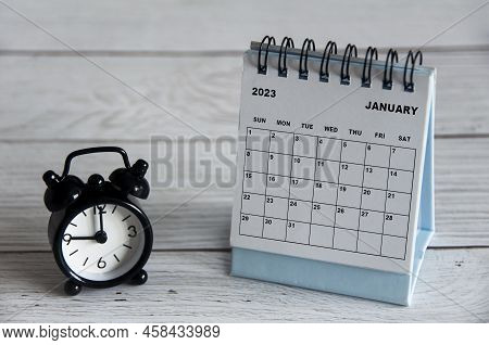 January 2023 White Desk Calendar With Black Alarm Clock Pointing At 9 O'clock On Wooden Table. Calen