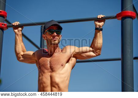Athletic Sportsman Trains On The Horizontal Bars. Training At The Open Air Sprorts Ground.