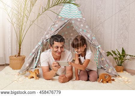 Indoor Shot Of Happy Family Spending Time At Home, Father With His Daughter Watching Cartoons Or Fun