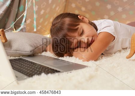 Indoor Shot Of Sleepy Little Dark Haired Girl Wearing White T Shirt Or Pajama Laying On Floor In Wig