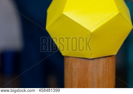 The Multifaceted Yellow Figure Is Made Of Many Yellow Paper Pentagons On A Wooden Stand. Selective F