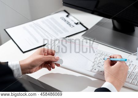 Businesswoman Holding Pen And Important Message Wtitten On Paper On Desk With Computer, Clipboard An