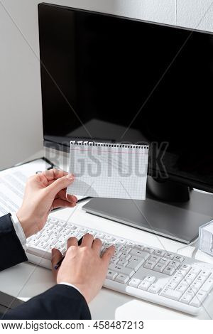 Businesswoman Holding Important Message Wtitten On Paper On Desk With Computer, Clipboard And Notes.