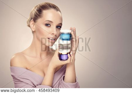 Pretty Woman With Clean Fresh Skin Hold A Different Of Face Care Creams, Wearing In Bathrobe. Expres