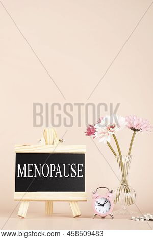 Menopause Word Written On Black Board, Flowers, Clock And Pills On Beige Background. Women Health An