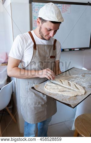 A Man In A Bakery Sends Traditional French Fougasse Bread Into The Oven. Vertical Photo.