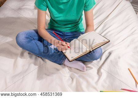 A Girl In A Green T - Shirt And Blue Jeans Is Sitting On The Bed And Writing In A Notebook , Colored