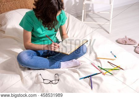 A Girl In A Green T - Shirt And Blue Jeans Is Sitting On The Bed And Writing In A Notebook , Colored
