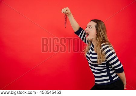 Shouting Aggressive Active Woman In Stripes Shirt Hold Red Hot Pepper At Arm Lenghth In Red Studio. 