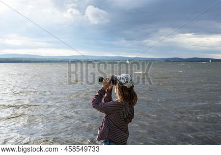 Young Woman In Cap Looking Through Binoculars At Birds On The Lake Or River Birdwatching, Zoology, E