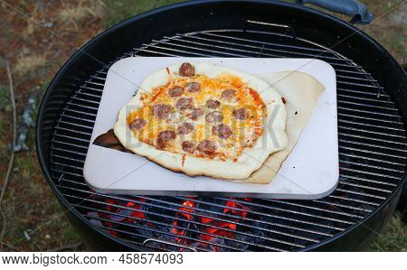 A Fresh Made Homemade Saussage Pizza Cooking On A Pizza Stone On A Charcoal Grill.