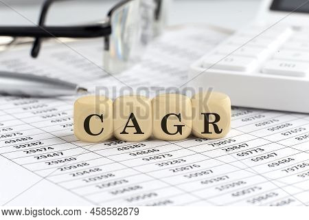 Wooden Cubes With The Word Cagr On A Financial Background With Chart, Calculator, Pen And Glasses, B