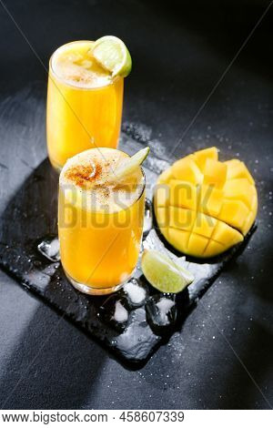 Two Mangonada Summer Cocktails On A Dark Background With Ice And Lime Slices. Top View
