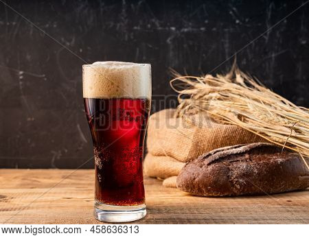A Glass Of Dark Beer. Beer, Wheat And Dark Bread. Dark Beer And Bread On A Wooden Table. A Glass Of 