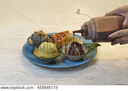 Hands Pouring Chocolate Toping On  Homemade Ice Cream With Waffle On Plate With Chocolate Syrup