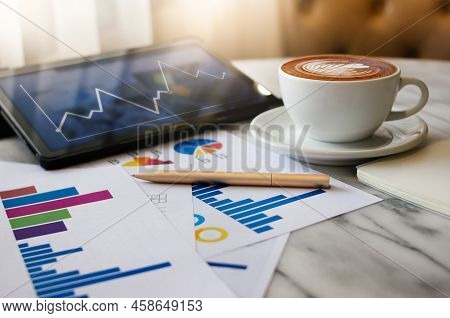 Close Up View, Latte Coffee In White Cup With Pen, Chart Of Investment And Tablet Computer On Table 